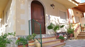 A building with a wooden door, a green metal staircase, and potted plants. - Villa Rahal (Racalmuto)
