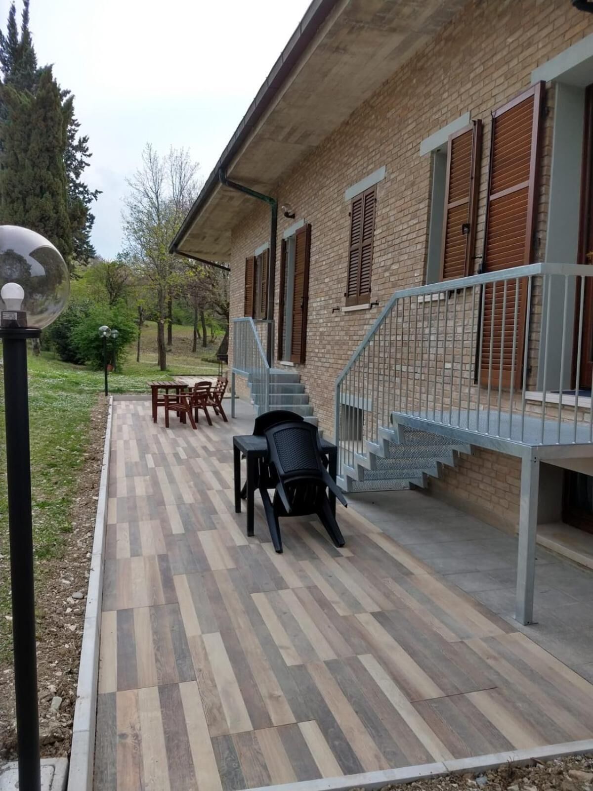 A covered patio area with a wooden deck, outdoor furniture, and a staircase leading to a balcony.