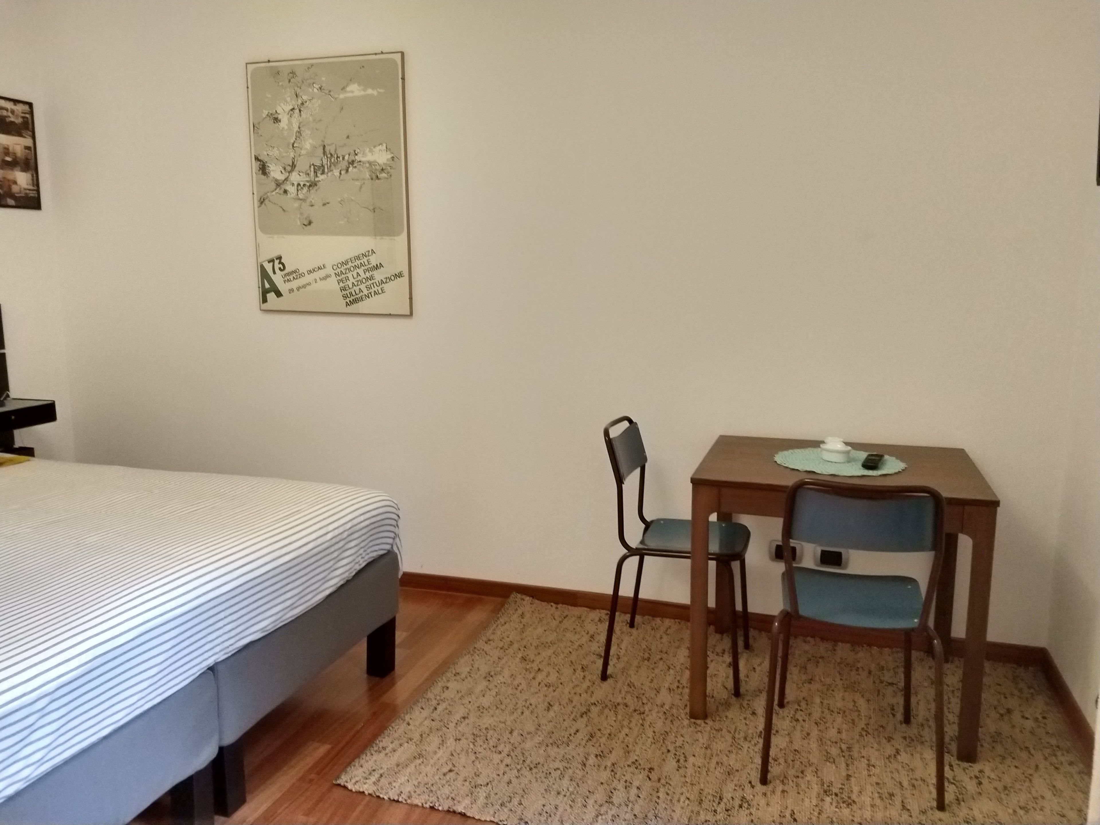 A bedroom with a bed, a desk, two chairs, and a poster on the wall.