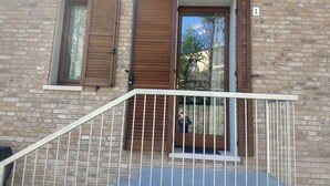 A brick building with a balcony, a door with wooden shutters, and a window with a metal grill. - B&B Il Torchio (Urbino)