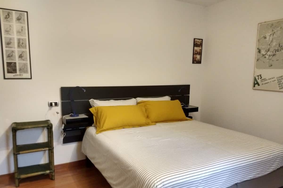 A bedroom with a bed, a nightstand, a lamp, and a framed picture on the wall.