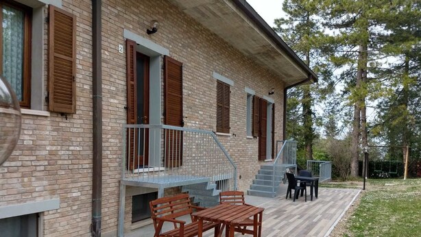 A brick house with a balcony, wooden furniture, and a staircase leading to the upper floor. - B&B Il Torchio (Urbino)
