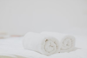 Two rolled white towels on a white surface.