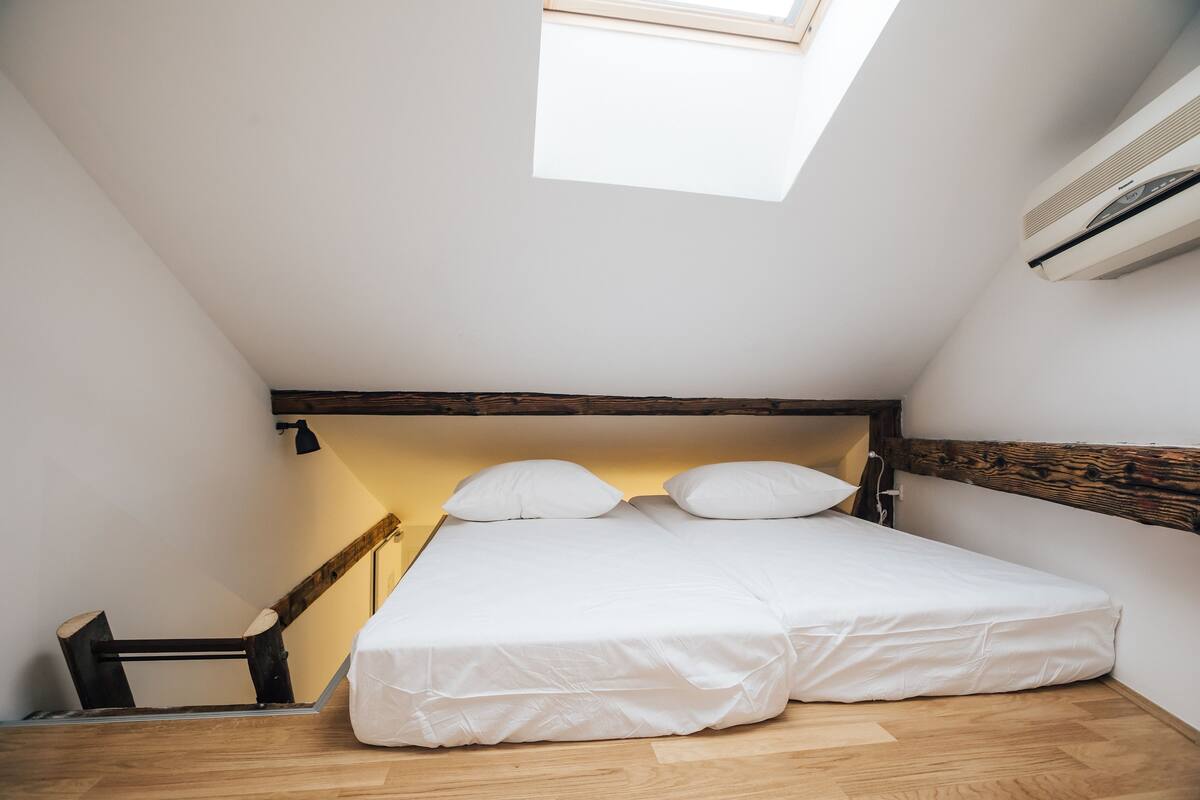 Een kleine, goed verlichte slaapkamer met een schuine kap, dakraam en een bed met witte beddengoed.