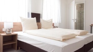 A double bed with white linens, a bedside table with a lamp, and a TV on the wall. - Grüner Baum (Langenau)