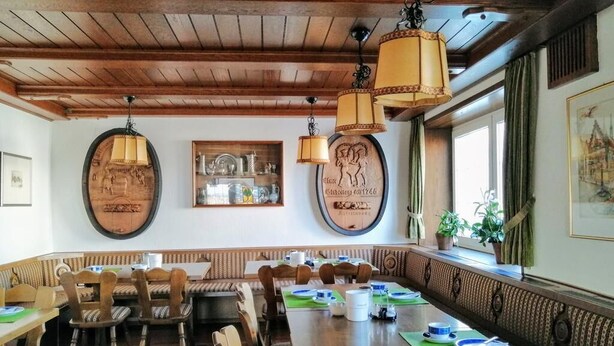 A dining area with wooden tables and benches, pendant lights, and framed artwork on the walls. - Grüner Baum (Langenau)