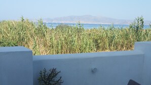 Een terras met uitzicht op zee en verre bergen, met een witte muur en een kleine potplant.