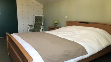 A single bed with a wooden frame and white bedding, a chair with a polka dot pattern, a small table with a lamp, and a wall with a simple pattern.