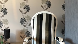 A striped armchair in a room with floral wallpaper and a wooden side table. - Maison d'hotes La Colombelle (Colombé-le-Sec)