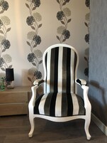 Un sillón a rayas en una habitación con papel tapiz floral y una mesita de madera.
