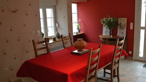 A dining area with a red tablecloth, wooden chairs, a vase, and a welcome sign. - Maison d'hotes La Colombelle (Colombé-le-Sec)