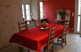 Un comedor con mantel rojo, sillas de madera, un jarrón y un letrero de bienvenida.