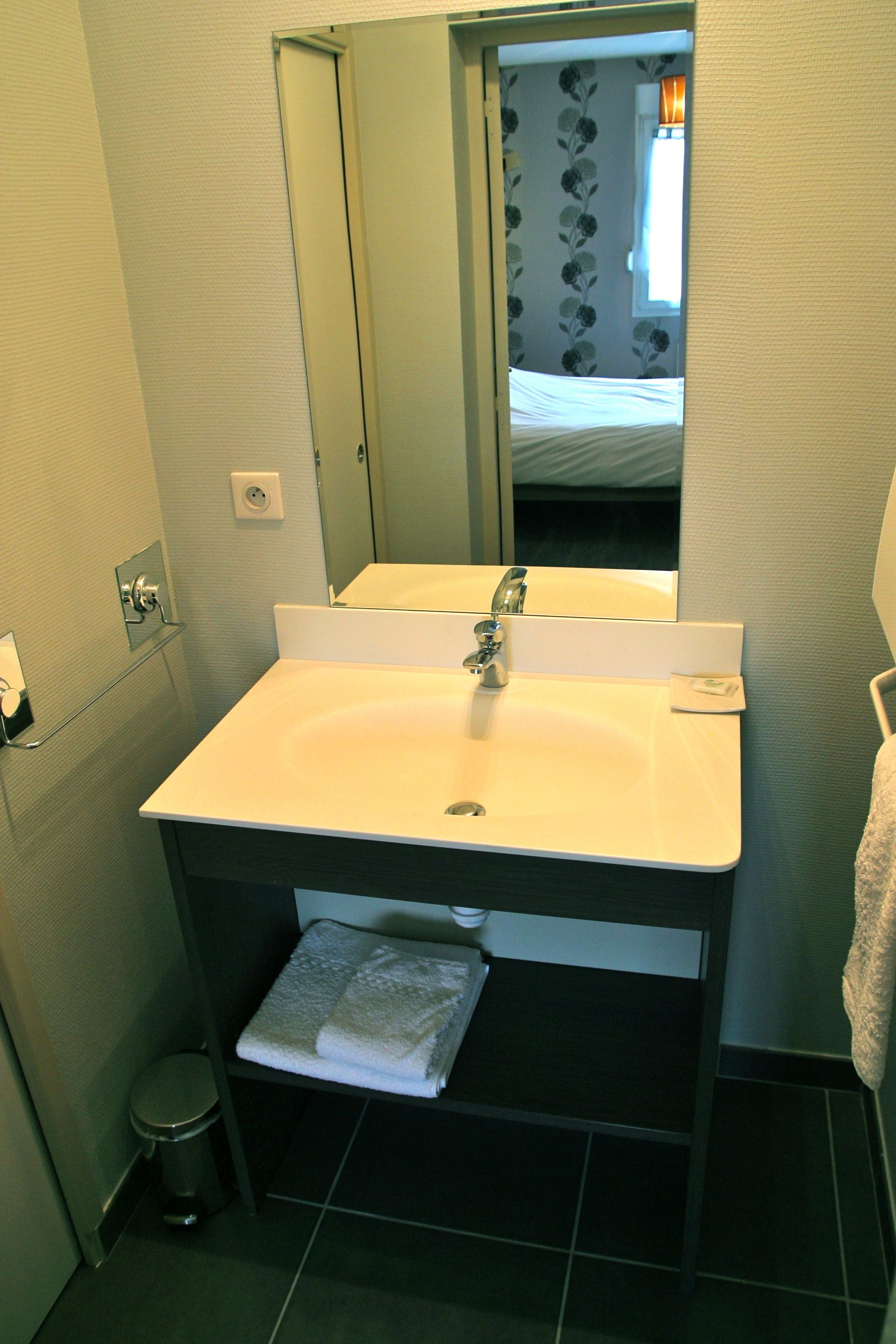 A bathroom with a white sink, a mirror, a towel rack, and a small trash bin.