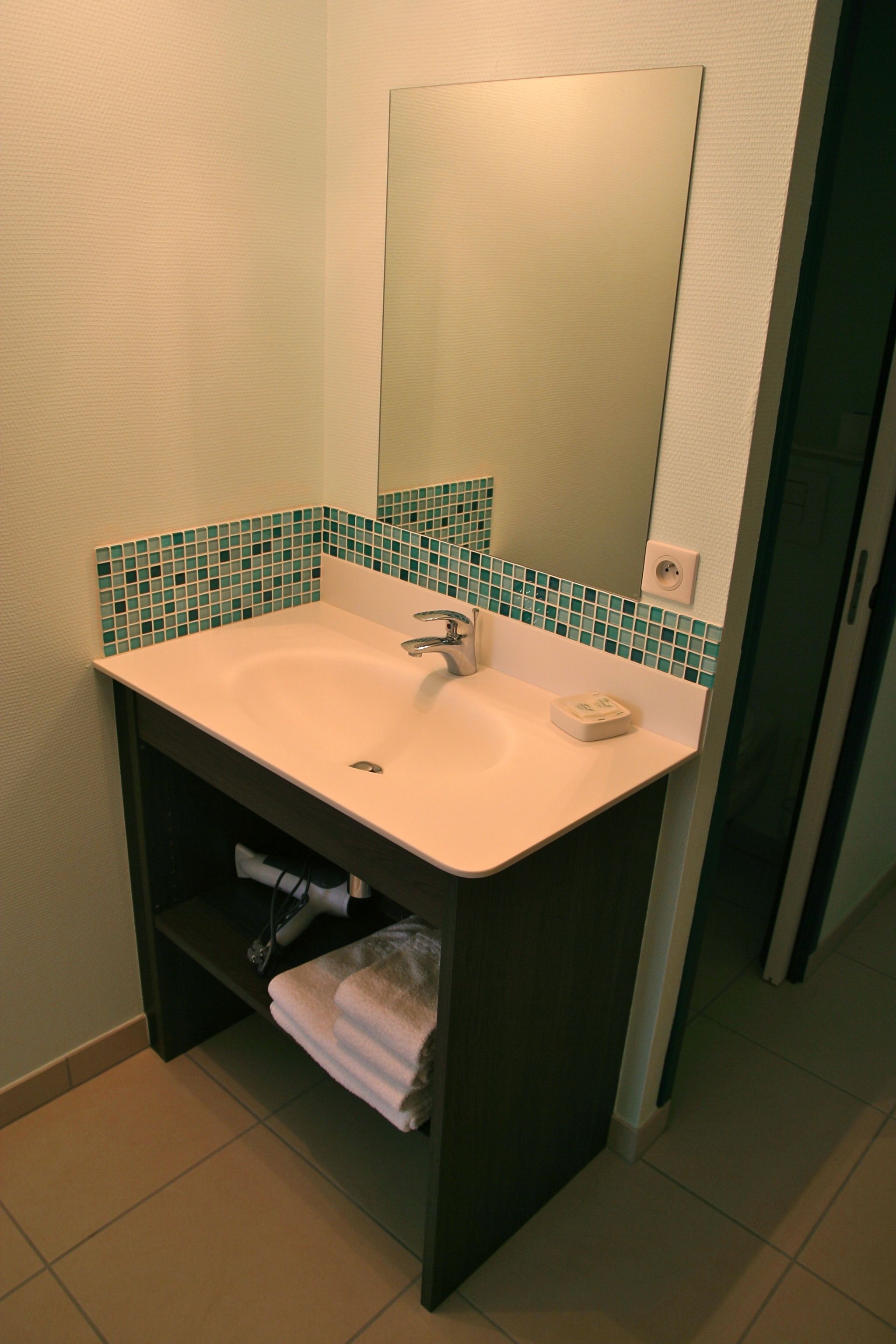 Een badkamer met een witte wasbak, een spiegel en een groene tegeltjeswand.