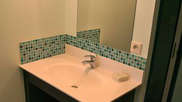 Een badkamer met een witte wasbak, een spiegel en een groene tegeltjeswand.