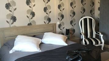A neatly made bed with white and gray bedding, a black handbag on the bed, and a black and white striped chair.