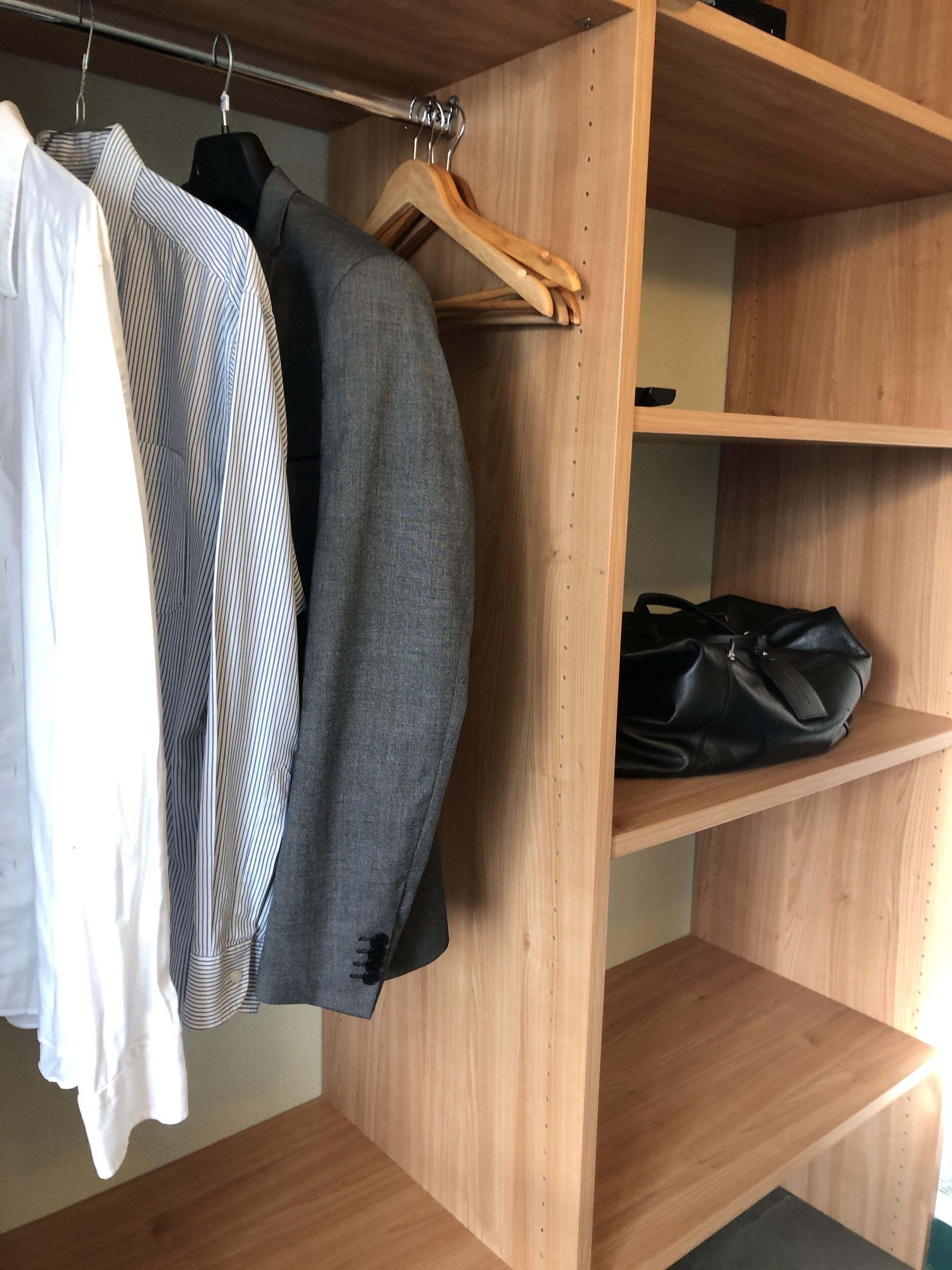 Un armario de madera con ropa colgada y un bolso negro.