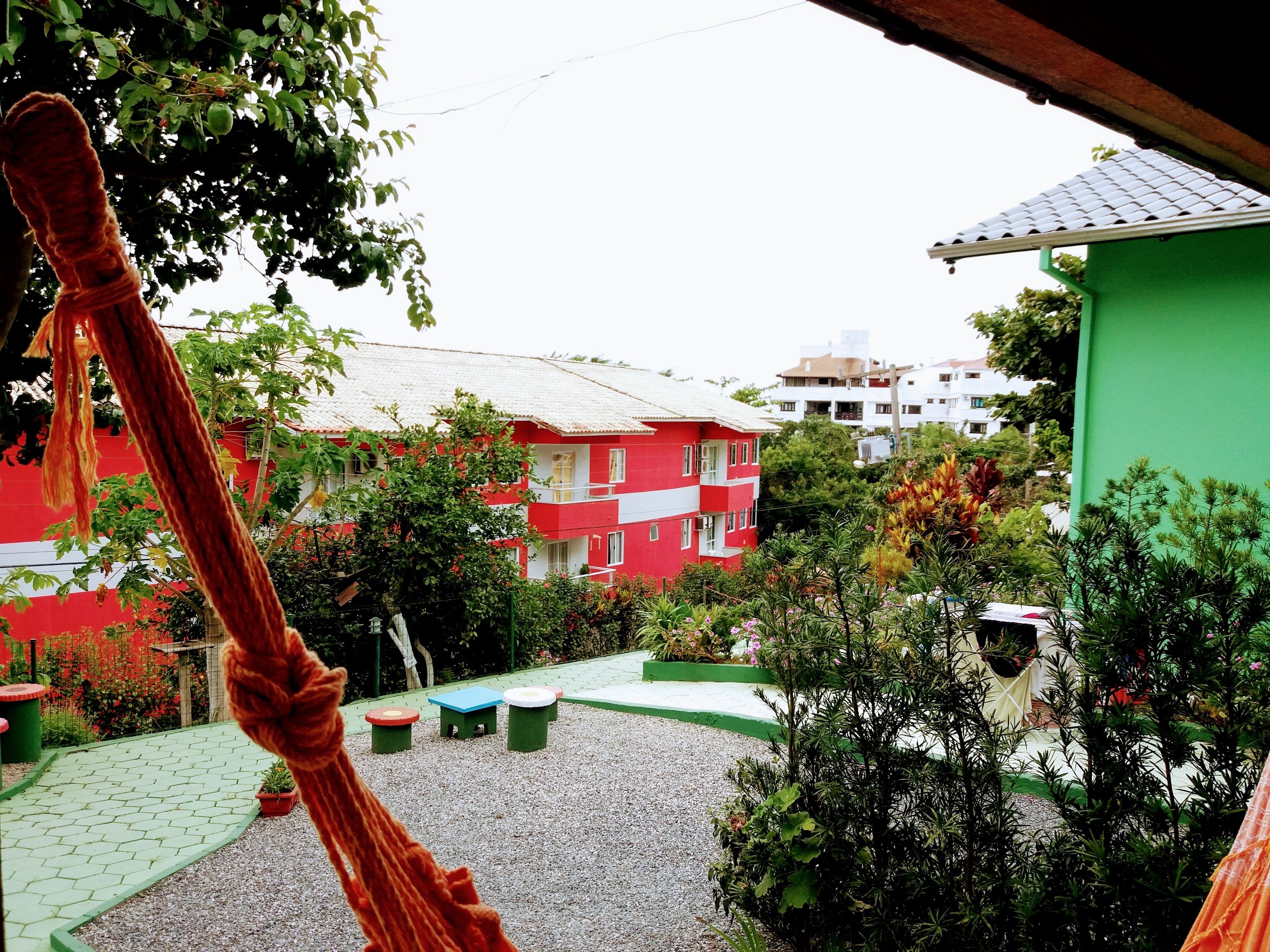 Ein rotes Gebäude mit einem weißen Balkon, umgeben von Grünflächen und einer gepflasterten Fläche mit Bänken.