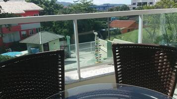 A balcony with wicker chairs and a glass table, overlooking a residential area with houses and greenery.