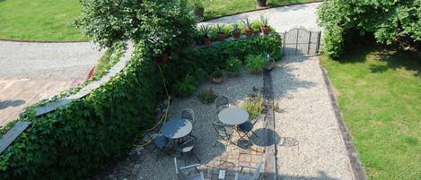 Un patio al aire libre con un sendero de grava, rodeado de abundante vegetación y plantas en macetas.