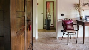 Una puerta de madera con picaporte rojo, una silla con asiento de cuero, un florero con plantas secas y un cuadro enmarcado sobre una mesa.