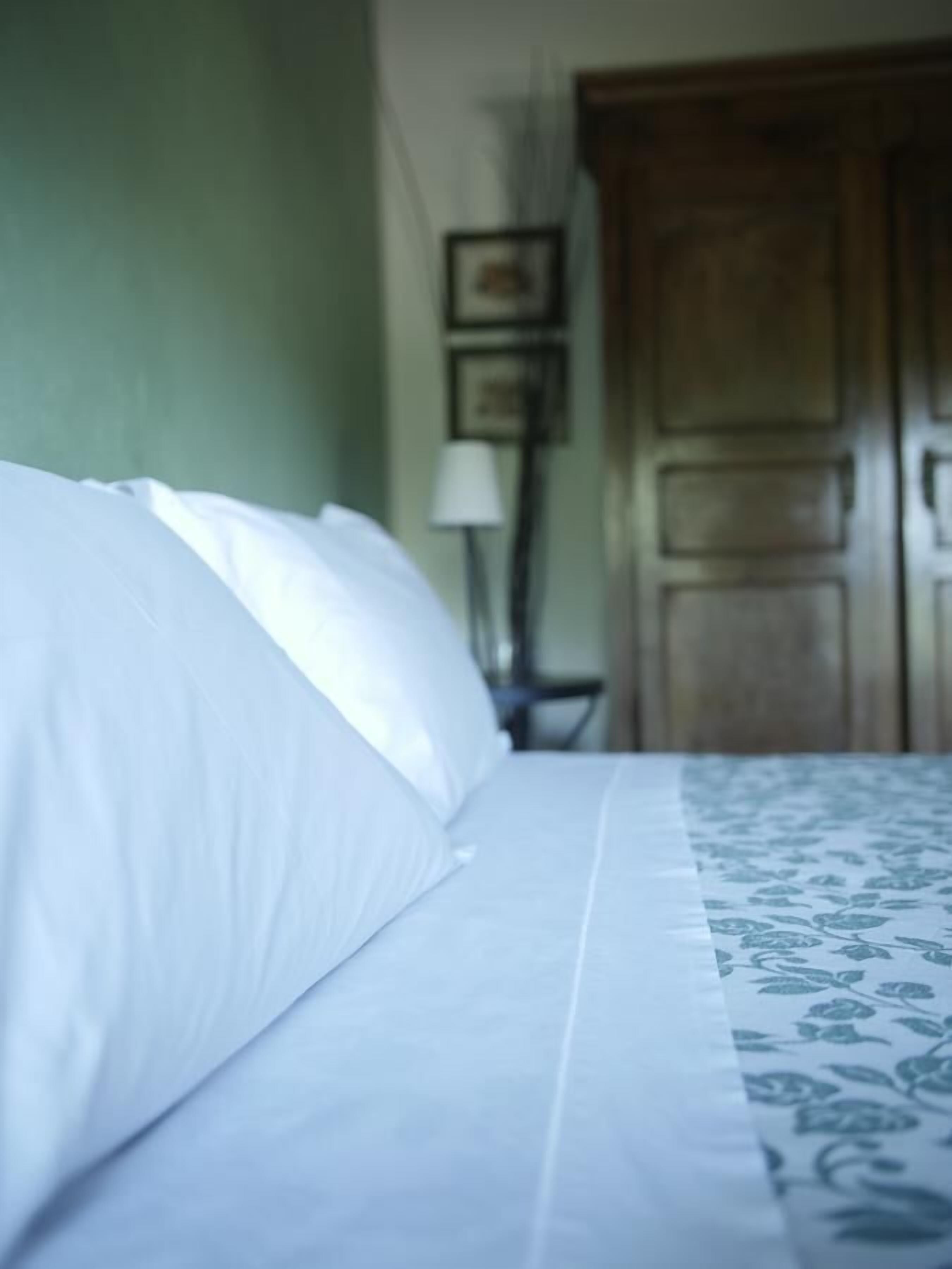 Una cama con ropa de cama blanca y una cubierta con estampado floral. Se observa un armario de madera al fondo.