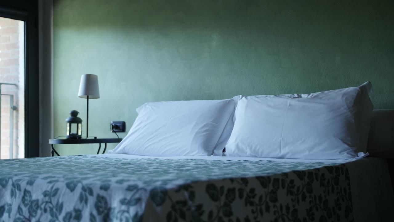 Ein Bett mit weißen Leinentüchern, eine grüne Wand, eine Lampe und ein kleiner Tisch mit einer Lampe darauf.