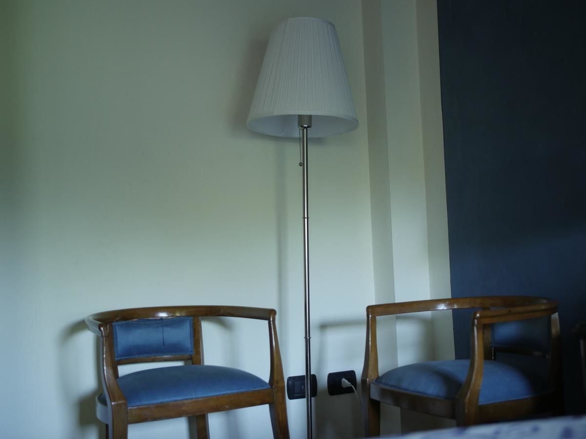 Dos sillas de madera con cojines azules, una lámpara de pie y parte de una pared oscura.