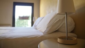 Una cama bien tendida con sábanas blancas, una lámpara de noche y vistas a un balcón a través de una puerta abierta.