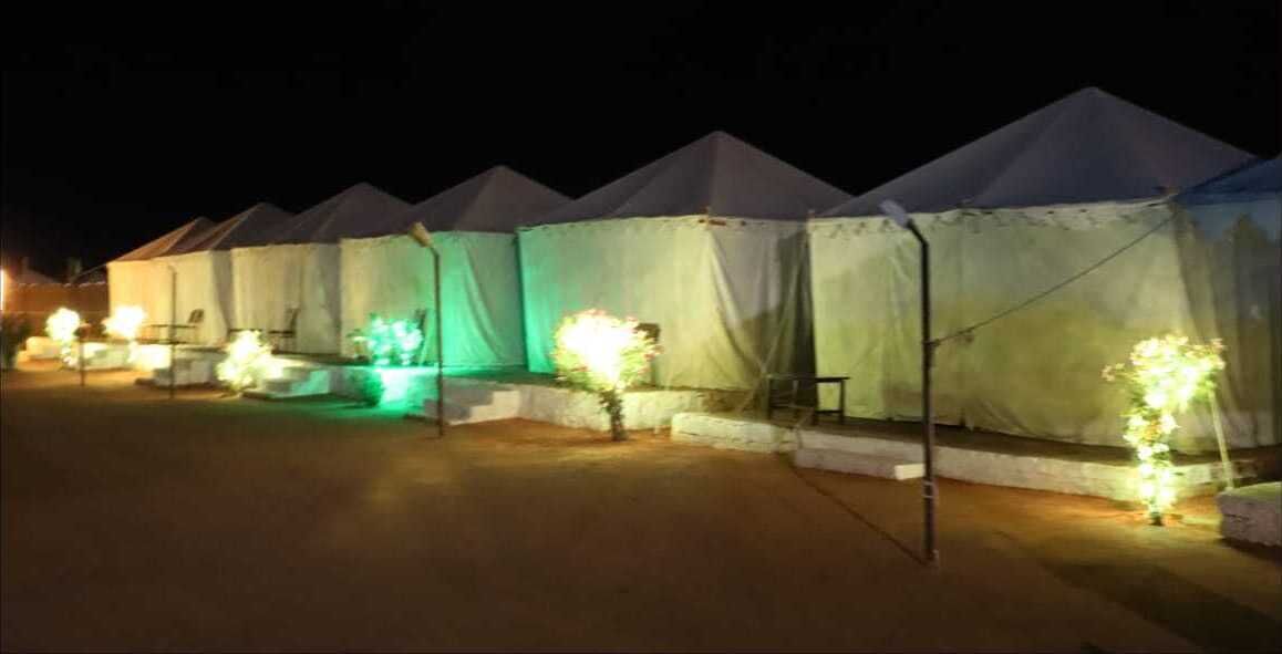 Filas de tiendas de campaña con escalones que conducen a la entrada, iluminadas por luces.