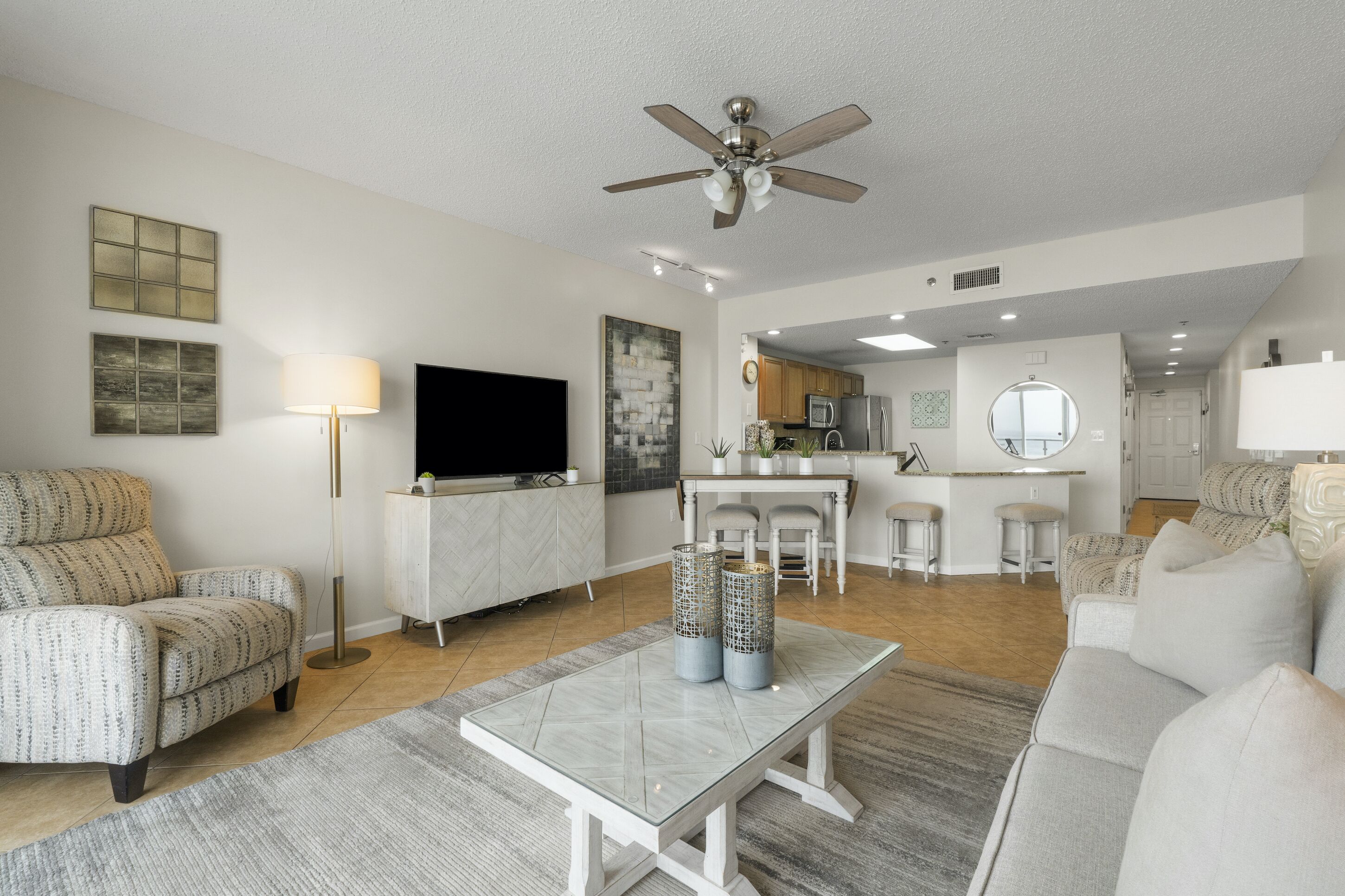 A modern living room with a sofa, a coffee table, and a TV. There is a kitchen area in the background.