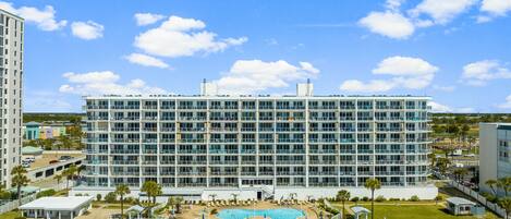 A multi-story hotel with a swimming pool and beach access.