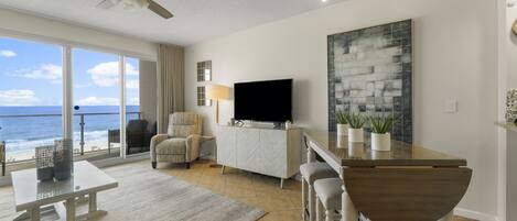 Una sala moderna con un televisor grande, un comedor y un balcón con vistas al océano.