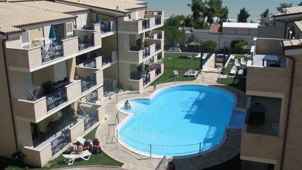 A multi-story hotel with a swimming pool, balconies with outdoor furniture, and a view of the sea. - Green Bay Village (Pineto)