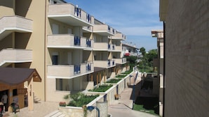 A multi-story hotel with balconies, outdoor seating, and a small garden area. - Green Bay Village (Pineto)