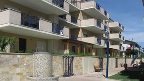 A multi-story residential building with balconies, a stone wall, and a paved courtyard. - Green Bay Village (Pineto)