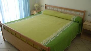A bed with a wooden frame and green bedding, a nightstand with a lamp, and a window with curtains.