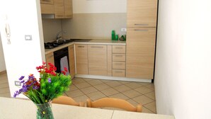 A kitchen with wooden cabinets, a sink, and a stove. There is a vase with flowers on the table. - Green Bay Village (Pineto)