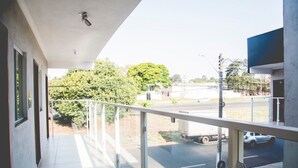 A balcony with a metal railing, a tiled floor, and a view of a road with vehicles and trees in the background.