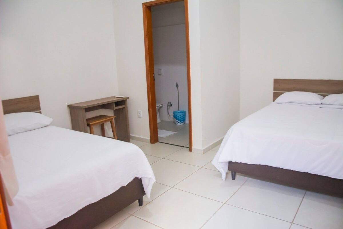 Una habitación de hotel con dos camas, una mesita de noche de madera y un baño visible a través de una puerta abierta.