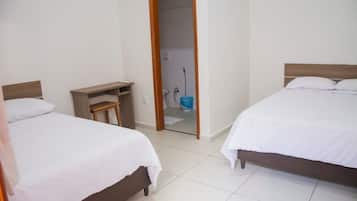 Una habitación de hotel con dos camas, una mesita de noche de madera y un baño visible a través de una puerta abierta.