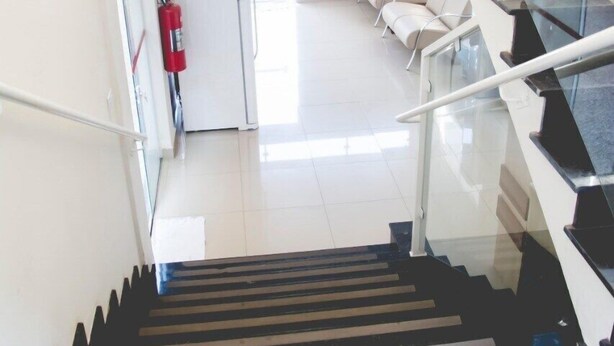 A modern interior with a staircase leading to a lower level, a white wall with a fire extinguisher, and a seating area with white chairs.