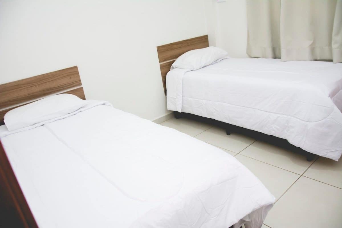 Dos camas individuales con cabeceros de madera en una habitación con paredes blancas y suelo de baldosas.