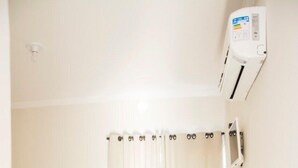A small, clean room with two beds, a wooden cabinet, a curtain, and an air conditioning unit.