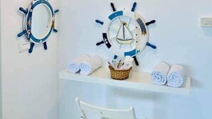 A bathroom with a white wall, a ceiling light, two ship's wheel wall decorations, a shelf with towels, and a white chair. - Kenting Trail Villa (Hengchun)