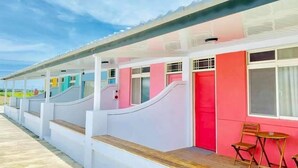 A row of single-story buildings with a covered walkway, each with a distinct color scheme and a small seating area with a table and chairs. - Kenting Trail Villa (Hengchun)