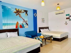 Habitació d'hotel amb dos llits, un butac armchair blau, una taula petita i una decoració mural amb temàtica de platja.