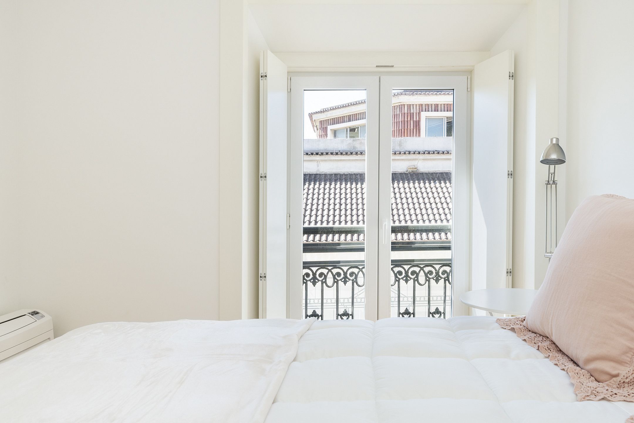 A bedroom with a bed, a nightstand, a lamp, and a view of a balcony with a railing.