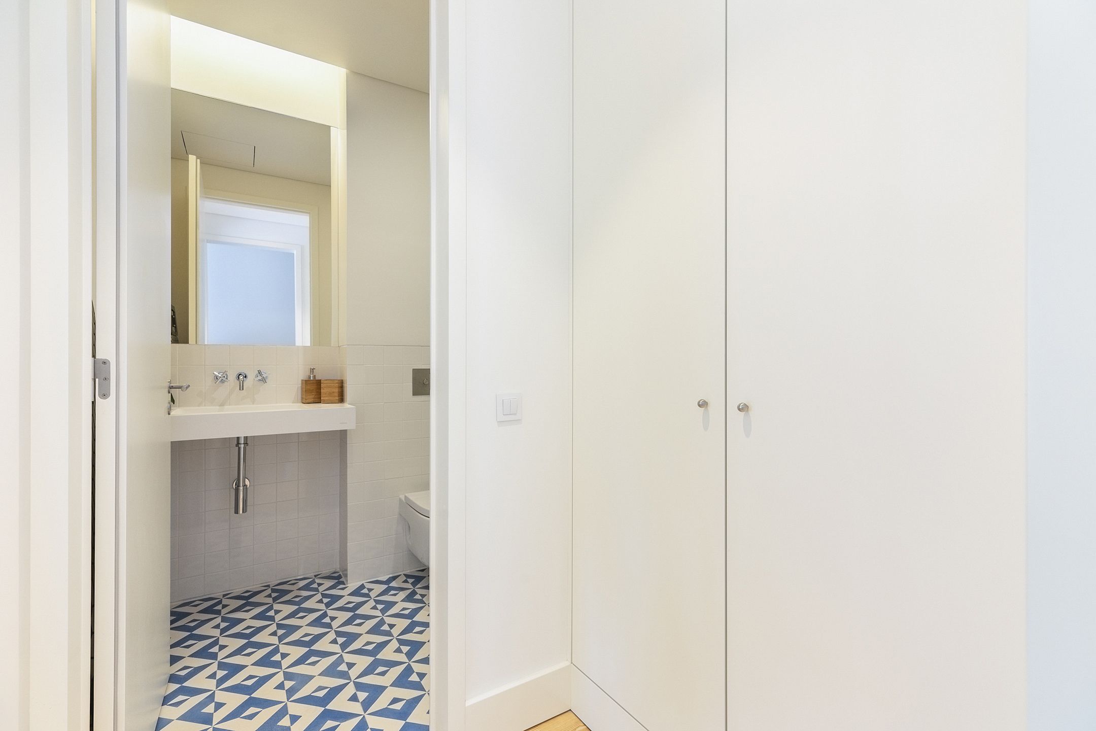 Un baño con lavamanos blanco, espejo y mueble, y un suelo con estampado azul y blanco.