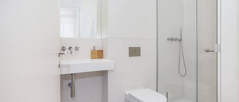 A modern bathroom with a white sink, toilet, and glass shower enclosure.